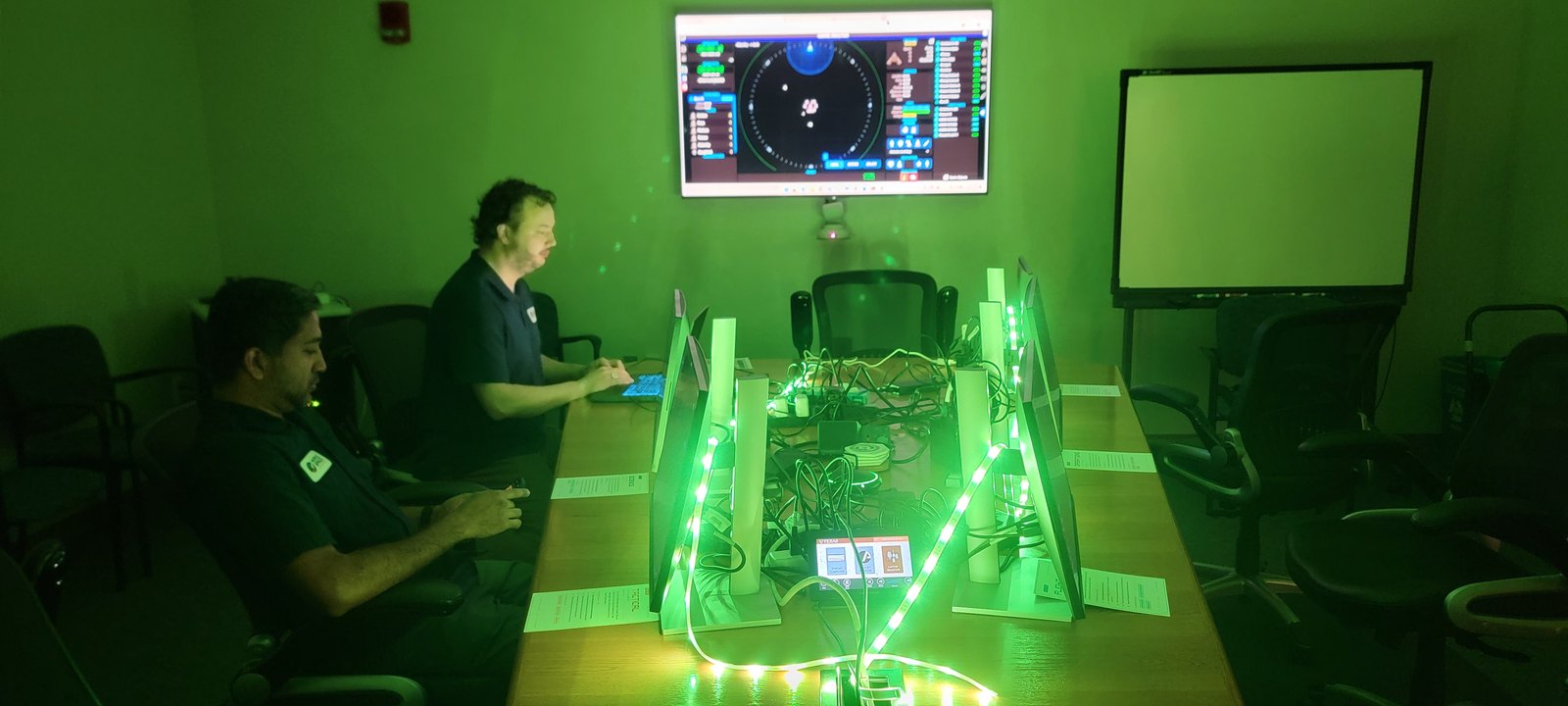 Two operators running pre-mission checks at green-lit bridge consoles beneath the main display