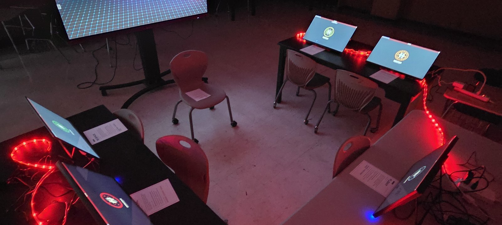Starship bridge consoles under red alert lighting set up in a school classroom with the main viewscreen showing a starfield